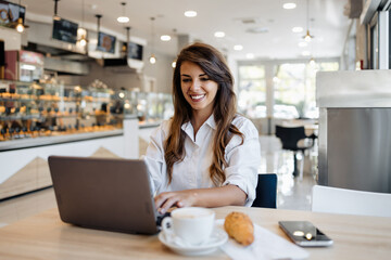 Beautiful and happy young woman sitting and eating delicious rolls in bakery or fast food while she...