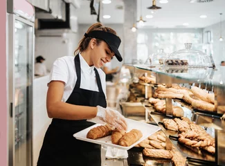 Tuinposter Beautiful young and happy female worker working in a modern bakery or fast food restaurant. © Dusko