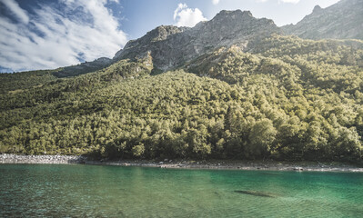 Mountain landscape with a cold mountain lake against the backdrop of a forest and a rocky peak in the mountains, a mountain reflection in the lake, a landscape in the mountains in a warm sunny summer