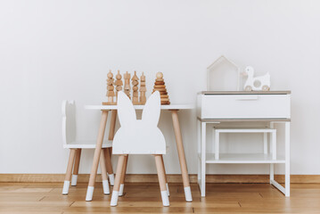 Fototapeta na wymiar Scandinavian child room with beige wall, stylish children's chair, table, bed and wooden toys. Modern interior. Copy space.