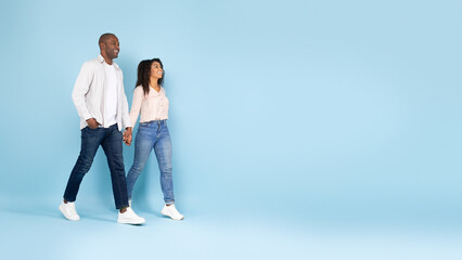Full length shot of african american couple holding hands and walking, looking at free space, blue...