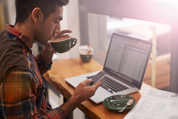 Life begins after coffee. a young man using his cellphone and laptop in a coffee shop.