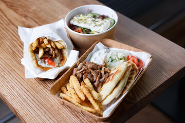 Greek fast food served for take away. Traditional pita souvlaki, gyros, Greek salad and pita with fries served in recyclable paper dishware on table. No people