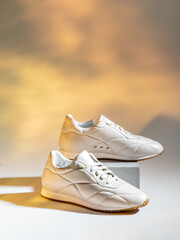A minimalistic closeup of stylish jogging footwear. Showcase of female elegant white sneakers on a cube platform with the beige background. The concept of modern lifestyle combining sport and style.