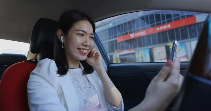 An Asian businesswoman is using her mobile phone inside the car to make a video call with colleagues or clients, demonstrating her flexibility and adaptability in conducting business remotely.	
