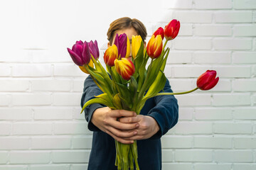 Unrecognizable boy holding a bouquet of tulips in front of a white brick wall