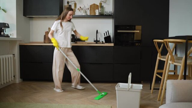 Carefree happy woman cleaning the living room at home is dancing merrily with a mop