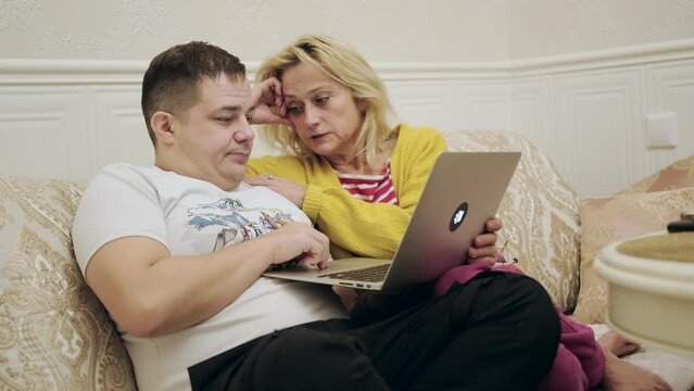 Mother and son are sitting on the sofa and enjoying the meeting while watching photos on the laptop in a comfortable home environment