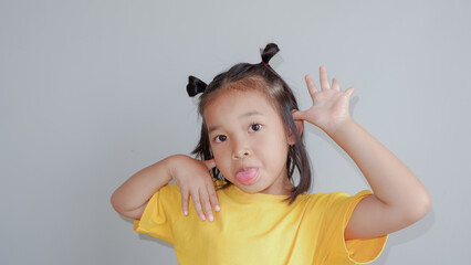 Image of little Asian child wearing yellow tshirt posing on gray background. making face concept..