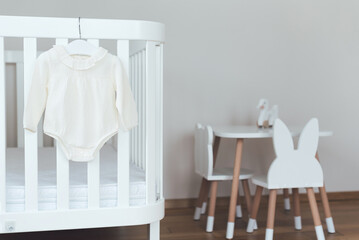 Wooden furniture set for kid. Baby bodysuit with hanger on bed in child room.