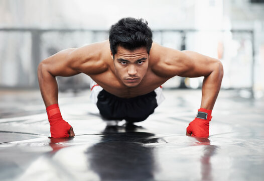 Push-ups are a must for any boxer. A focused young boxer doing push-ups in the gym.