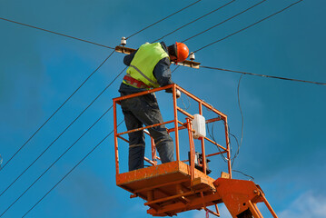 Electrician worker in crane cradle repairs electrical wires. Man repair broken electric cable at...