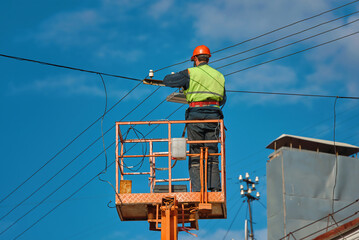 Worker in lifting cradle install led lantern on electric wires at height on city street. Man in...