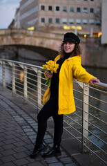 woman with a bouquet of spring daffodils in her hands, walks along the bridge in the evening