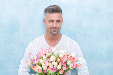 cheerful man with spring tulips in studio. man with spring tulips isolated on blue background.