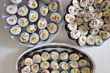 Plates with homemade sushi rolls on white table. Tuna and vegetable sushi, and vegetarian cream cheese and vegetable sushi. Top view.
