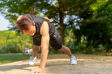 sporty handsome Asian man doing one arm push up bodyweight exercise in city public park on summer...