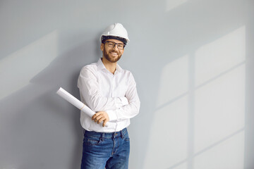 Happy young man architect or construction engineer in white shirt, safety hard hat, and eyeglasses...
