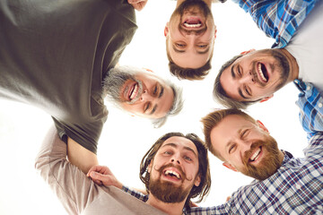 Team of men huddling. Group of male friends hugging. Bottom view of five happy young and mature bearded men standing head to head in circle, looking down at camera, smiling, laughing, and having fun