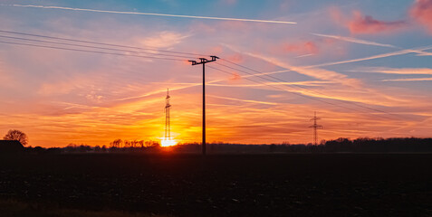 Sunset with a dramatic sky and overland high voltage lines near Tabertshausen, Bavaria, Germany