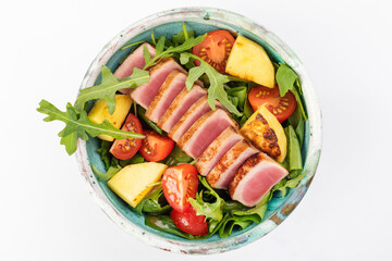 Poke bowl with tuna, cherry tomatoes, arugula, spinach, herbs, fried pineapples and soy sauce. Round bowl on a white background. Top view.