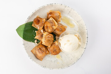 Bananas in rice paper with cinnamon, Jerusalem artichoke syrup, peanuts and ice cream. White ceramic plate on a white background. Top view.