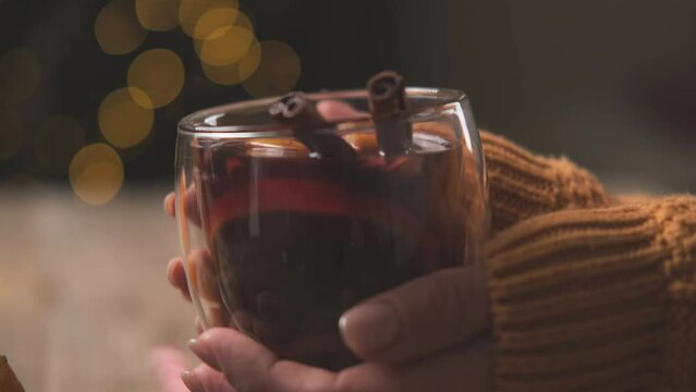 Woman holding transparent glass with mulled wine and cinnamon sticks