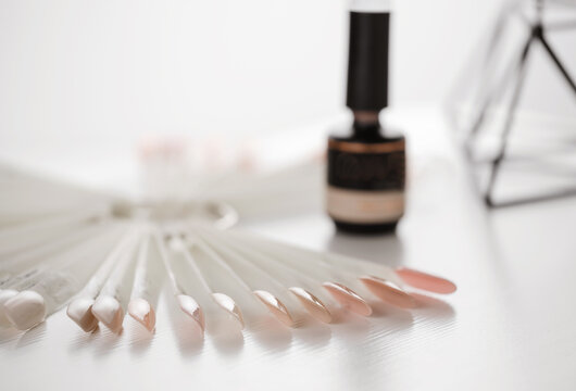 Gel lacquer bottle standing at table. Close up view of black bottle of nail polish standing at the white table at the nail salon near nude samples. Beauty routine concept, still life