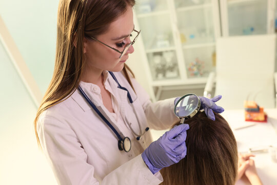 Female dermatologist checks health of her patient's hair and scalp with magnifying glass.