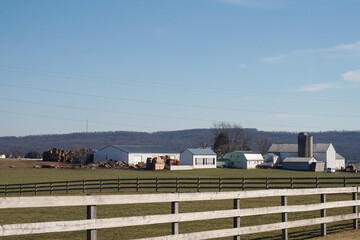 Fototapeta premium Farm Scene with White Fence and Buildings, Blue Sky, Green