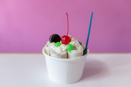 Close up of a rolled ice cream decorated with a cherry, a cookie and green bubble toppings
