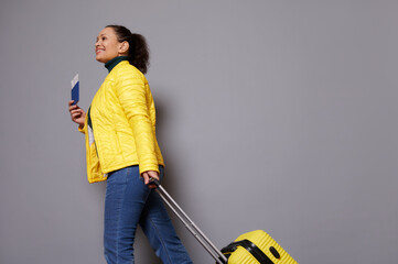 Bottom view of female traveler woman in yellow jacket and blue jeans, smiling while walking with...