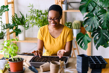 Young smiling african-american woman doing seed-starting early in the spring indoors for her...