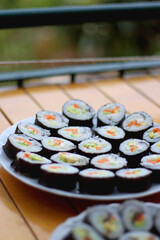 Plates with homemade sushi rolls on wooden table. Tuna and vegetable sushi, and vegetarian cream cheese and vegetable sushi. Selective focus.