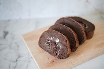 Chocolate roll cake slice with vanilla cream and dark compound chocolate. Sweets dessert cream roll chocolate snacks and food concept. Swiss Roll Cake, Cake roll on wooden