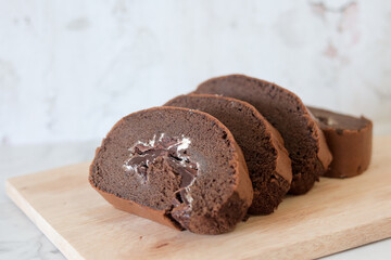 Chocolate roll cake slice with vanilla cream and dark compound chocolate. Sweets dessert cream roll chocolate snacks and food concept. Swiss Roll Cake, Cake roll on wooden