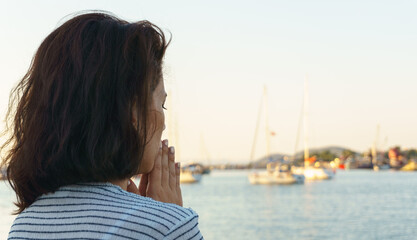 Young woman praying on beach. Blank copy space on sky and blue sea for advertising texts.