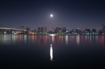 Obraz premium Tokyo skyline under full moon. Night photo with the modern skyscraper office buildings in Tokyo and Rainbow Bridge.