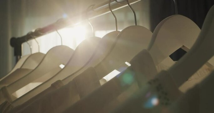 Rack with hangers of white clothes in the rays of the sun from the window
