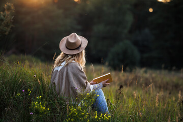 Woman is relaxing in nature and reading a book to improve her mindfulness and mental health - obrazy, fototapety, plakaty