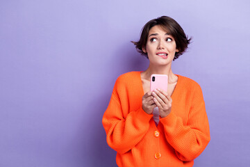Photo of nervous uncertain lady dressed orange cardigan chatting device looking empty space isolated purple color background - obrazy, fototapety, plakaty