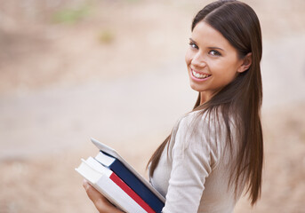 Fototapeta premium Ready to learn. A pretty young university student carrying textbooks on her way to class on campus.