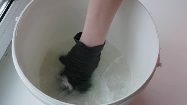 The hand dips the washcloth into the bucket of water and mixes with the powder