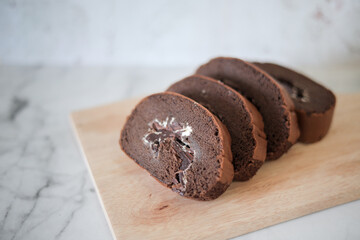 Chocolate roll cake slice with vanilla cream and dark compound chocolate. Sweets dessert cream roll chocolate snacks and food concept. Swiss Roll Cake, Cake roll on wooden