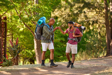 Obraz premium Two Male Friends With Backpacks Fist Bumping On Vacation Hiking Through Countryside Together