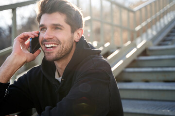Young hispanic adult talking on the phone otside with a beautiful smile during sunset