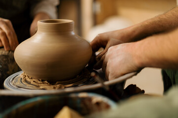 A potter in a pottery workshop removes a jug from the potter's wheel with a potter's knife