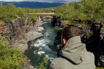 A man is enjoying the beautiful natural scenery in the north. Canyon and mountain river. Tourist attraction in Finland. Amazing scenic outdoor view. Travel, adventure, relaxed lifestyle