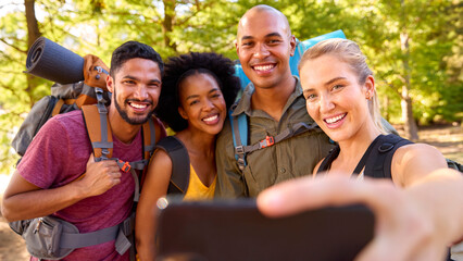 Group Of Friends With Backpacks Posing For Selfie On Mobile Phone On Vacation Hiking In Countryside
