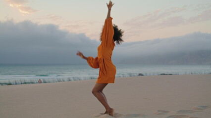 Contemporary dancer waving hands performing on sand seashore summer evening.